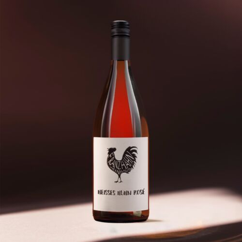 Eine Flasche Glüh-Huhn Rosé mit einem weißen Etikett mit schwarzer Hahngrafik und Text vor einem sanft beleuchteten braunen Hintergrund.