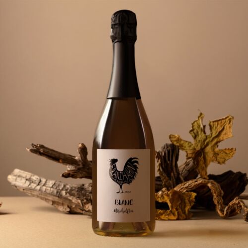 Eine Sektflasche mit der Aufschrift "Blanc" und dem Logo eines schwarzen Hahns steht auf einer beigen Fläche, umgeben von getrockneten Blättern und Holzstücken vor einem neutralen Hintergrund.
