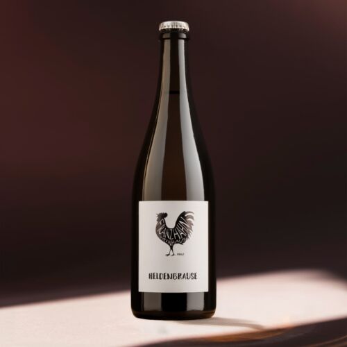 Eine dunkle Glasflasche mit einem weißen Etikett, auf dem ein schwarzer Hahn und der Text "HELDENBRAUSE" abgebildet sind, steht auf einer schwach beleuchteten Fläche vor einem verschwommenen braunen Hintergrund.