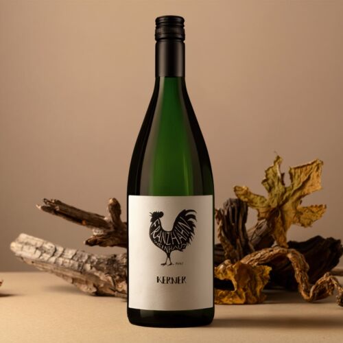 Eine grüne Weinflasche mit einem weißen Etikett, auf dem ein schwarzer Hahn und das Wort "Kerner" abgebildet sind. Die Flasche steht vor einem neutralen Hintergrund mit getrockneten Blättern und Holzstücken.