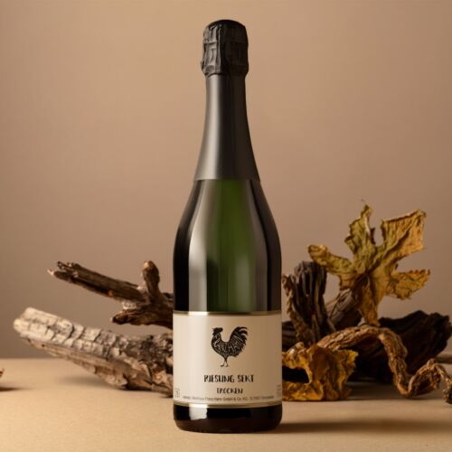 Eine Sektflasche mit der Aufschrift "Riesling Sekt Trocken" steht auf einer beigen Fläche, im Hintergrund sind getrocknete Blätter und Holzstücke arrangiert, die ein rustikales, herbstliches Bild ergeben.