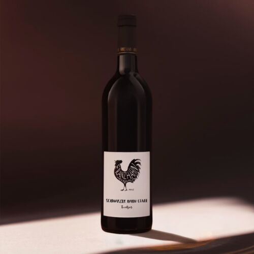 Eine Flasche Weiss Secco steht auf einer sonnenbeschienenen Fläche vor einem dunklen Hintergrund. Auf dem Etikett sind ein schwarzer Hahn und der Text "Weiss Secco" abgebildet.