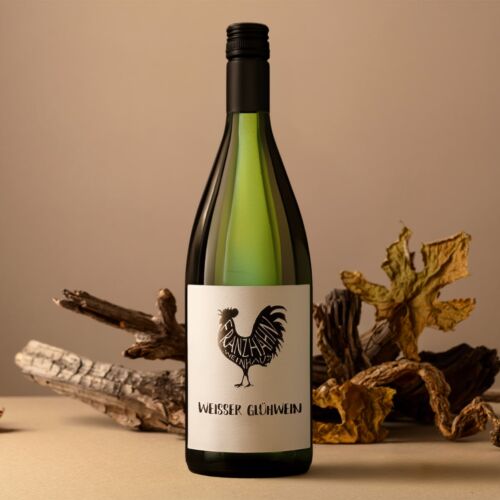 Eine Flasche Weißer Glühwein mit einem Hahn auf dem Etikett steht auf einer beigen Fläche, umgeben von Holzstücken und getrockneten Blättern vor einem neutralen Hintergrund.